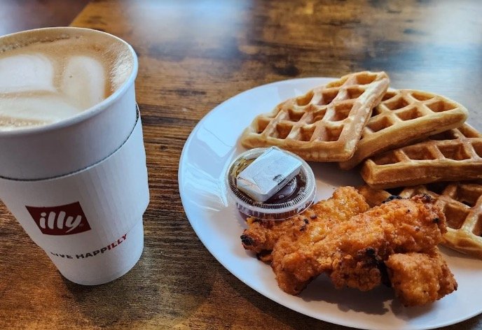 A latte beside chicken and waffles